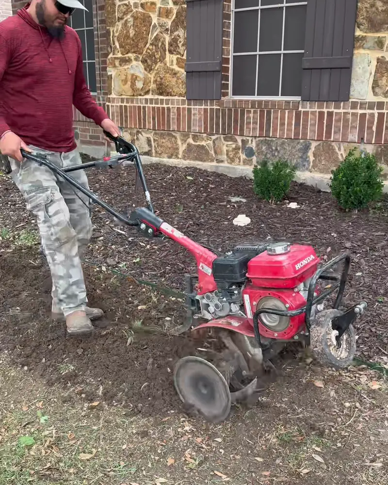 Crew member tilling a planting bed in front of a home